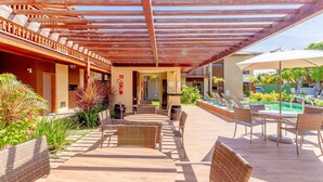 An outdoor patio with wicker furniture, a pool, and a covered area with wooden beams. - IT81 Great 3/4 Apartment (1 Suite) - Itacimirim (Camaçari)