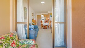 A living room with a sofa, a dining table with chairs, and a kitchen in the background. - IT81 Great 3/4 Apartment (1 Suite) - Itacimirim (Camaçari)
