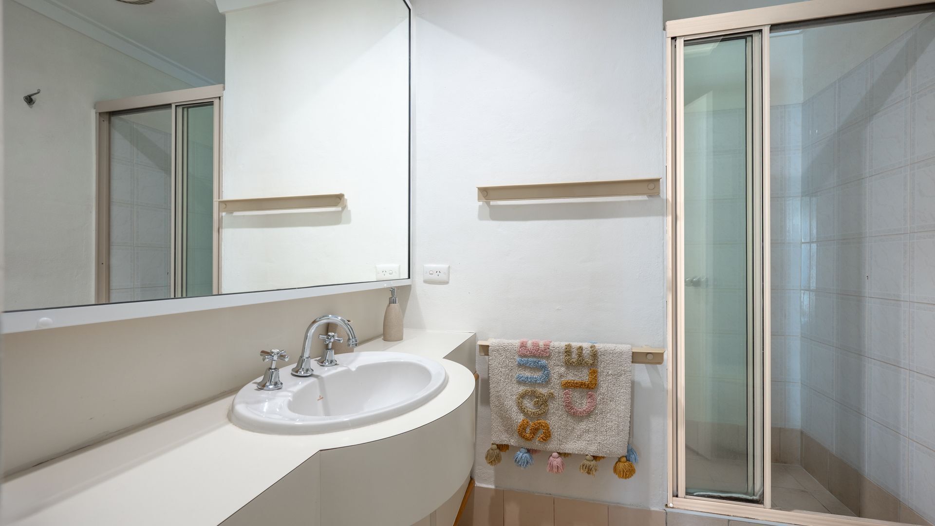 A modern bathroom with a white sink, mirror, and glass shower enclosure.