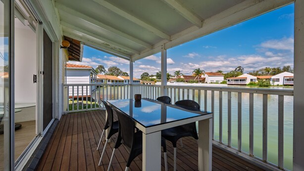 A covered outdoor area with a table and chairs, overlooking a body of water with houses in the background. - Escape to Tranquility at Fountain View Villa - South Yunderup (South Yunderup)