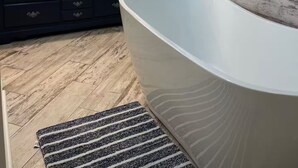 Un bany modern amb una banyera autònoma, un mirall gran i un penjador de fusta fosca amb diversos calaixos.