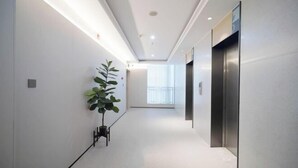 A modern hallway with a potted plant, an elevator, and a bright window at the end. - Homeinn · neo (Meishandong Railway Station Sansu Temple) (Meishan)