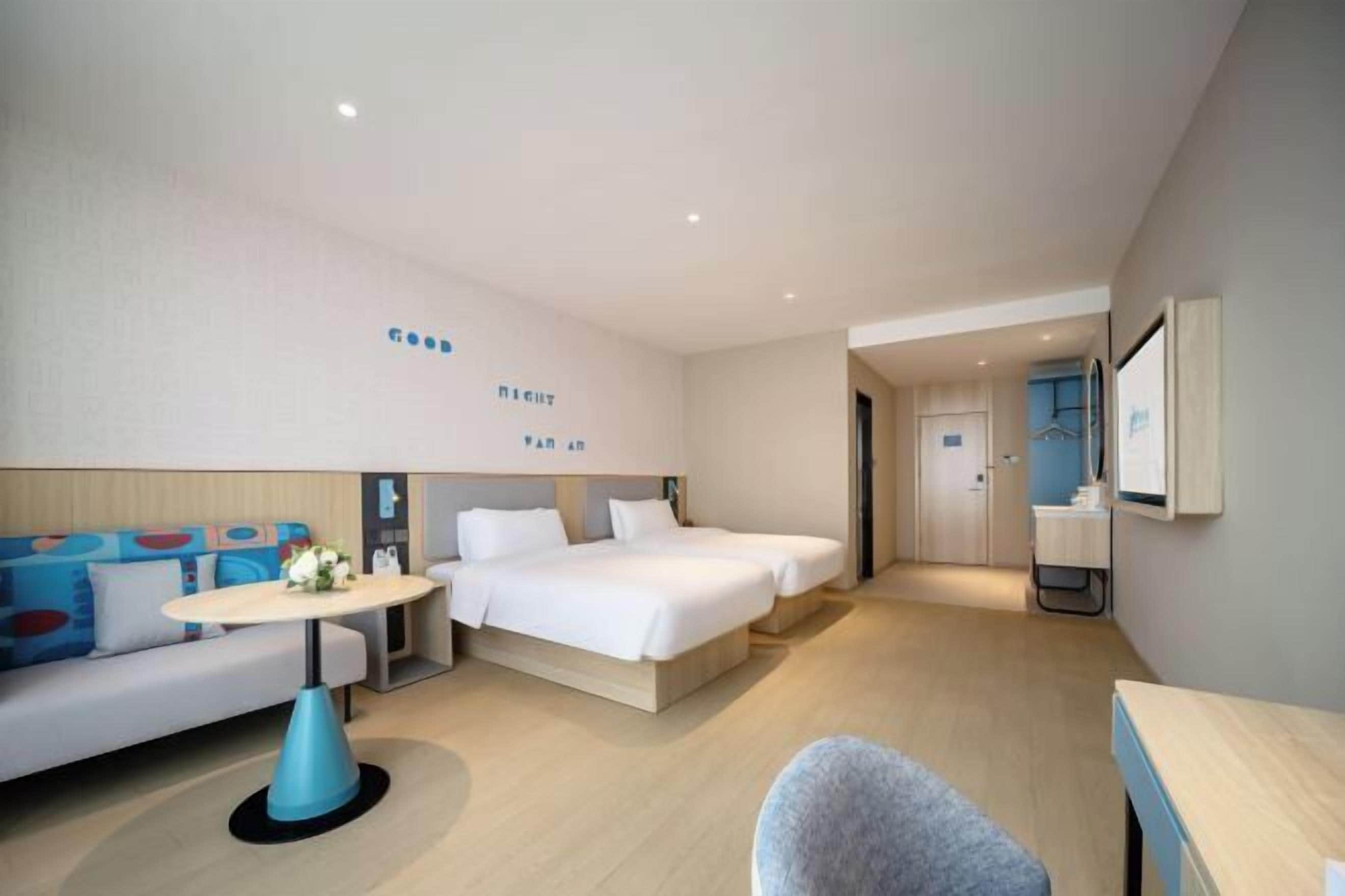 Een hotelkamer met een slaapbank, twee eenpersoonsbedden, een tafeltje en een stoel.