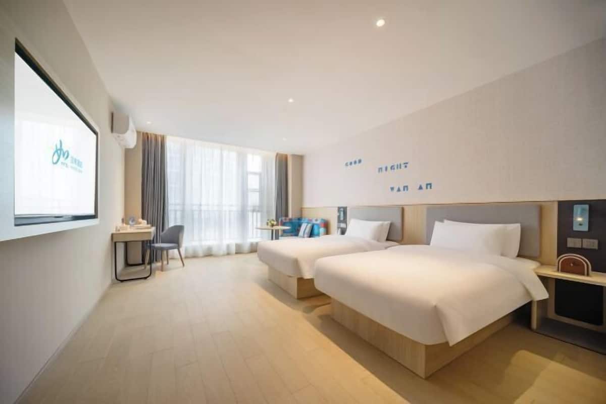Une chambre d’hôtel avec deux lits, un bureau, une chaise et une grande fenêtre.