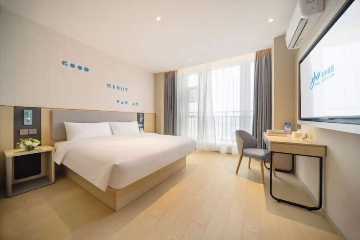 Une chambre d’hôtel comprenant un lit, une table de chevet, une chaise, un bureau et une grande fenêtre.