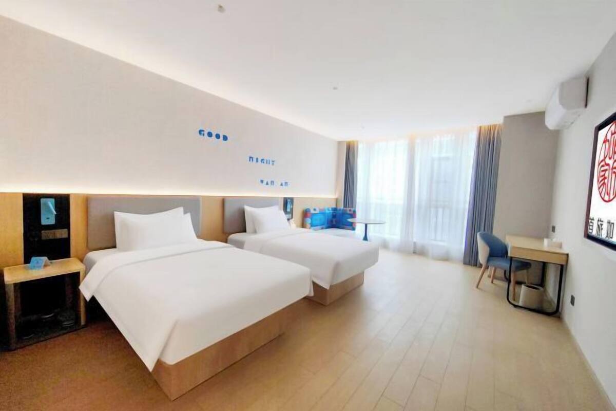 Une chambre d’hôtel avec deux lits, un bureau, une chaise et une grande fenêtre avec des rideaux.