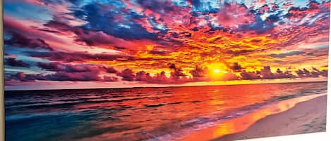 A painting of a sunset over the ocean with vibrant colors and clouds reflecting on the water.