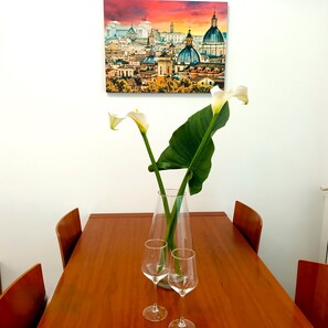 Une table à manger ornée d’un vase de fleurs blanches et de deux verres à vin.