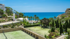 A tennis court with a clear view of the ocean and palm trees in the background.