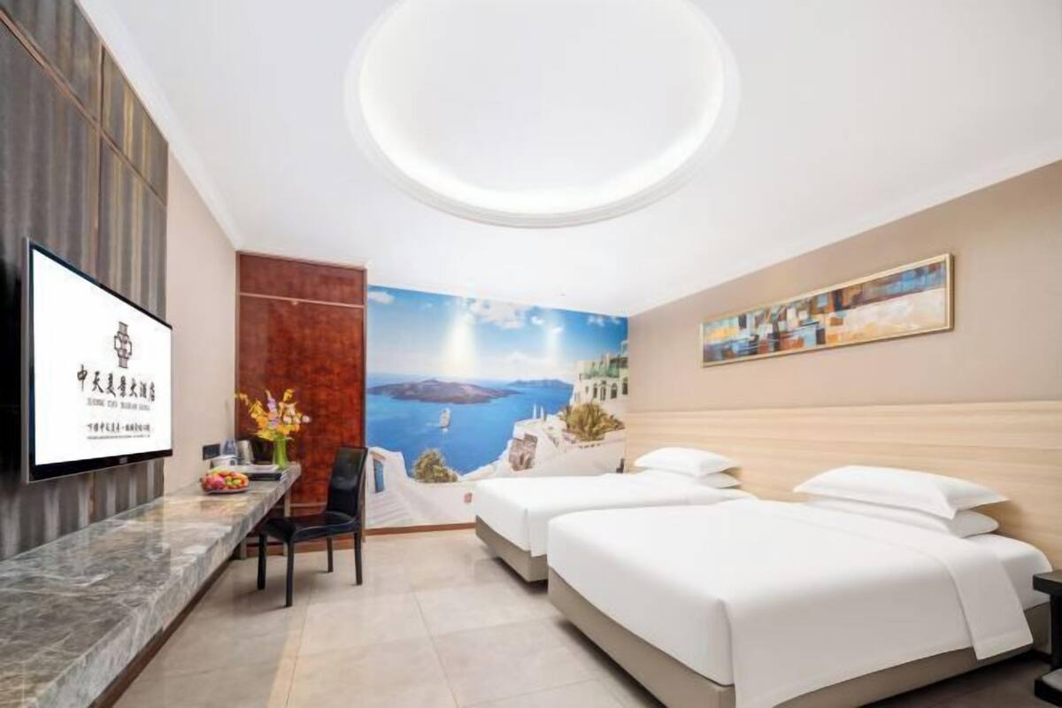 A hotel room with a marble reception desk, two beds, a large window with a scenic view, and a ceiling light fixture.