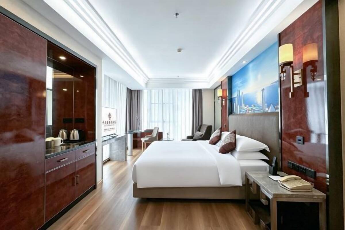A hotel room with a large bed, a desk, a chair, and a minibar.