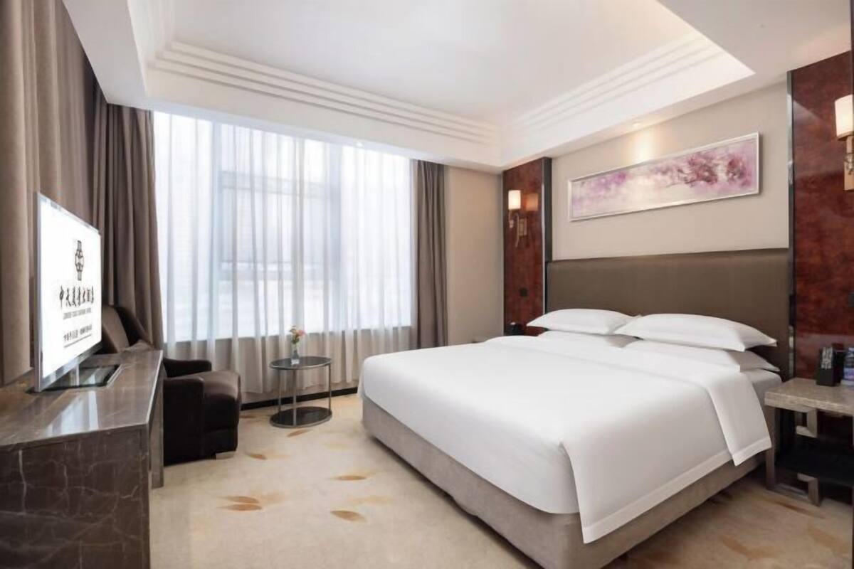 A hotel room with a large bed, a desk, a TV, and a window with curtains.