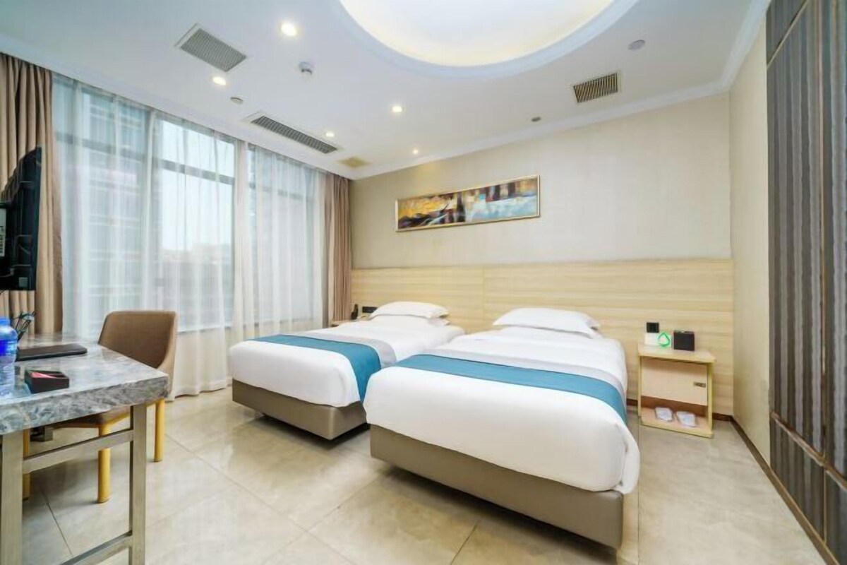 A hotel room with two beds, a desk, a chair, and a small bedside table.