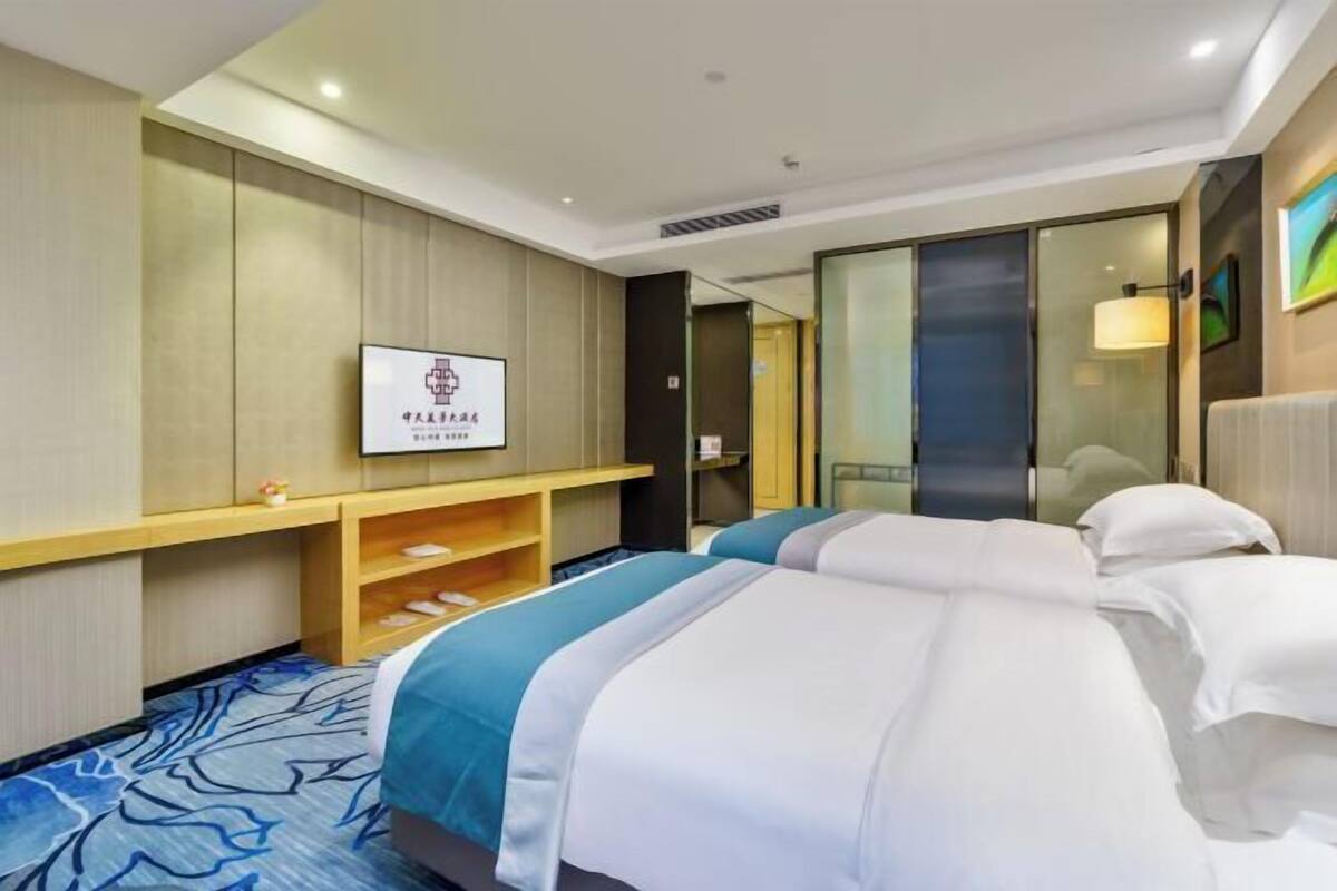 A hotel room with two beds, a wooden shelf, a flat-screen TV, and a large mirror.