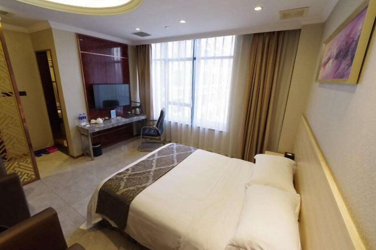 A hotel room with a large bed, a desk, a chair, a television, and a window with curtains.