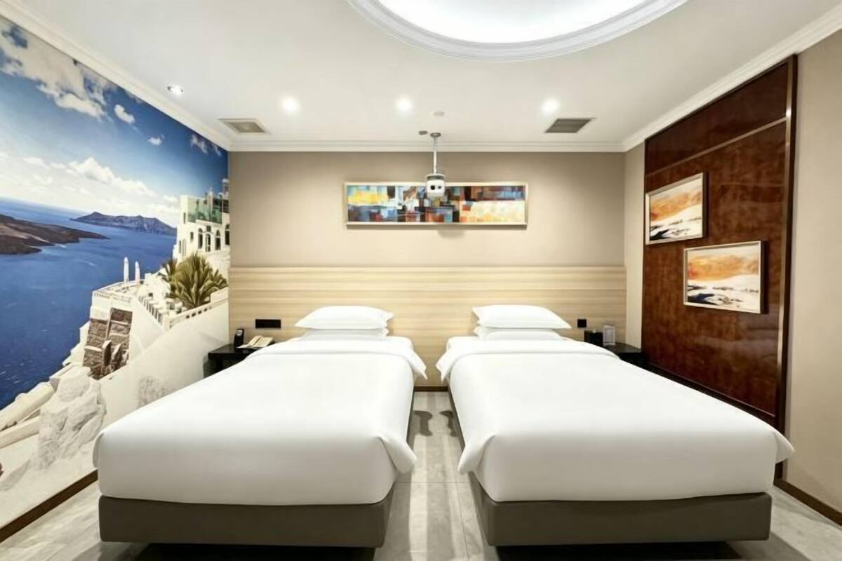 A hotel room with two beds, a mural of a coastal scene, a ceiling light, and artwork on the walls.