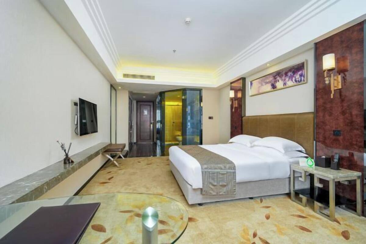 A hotel room with a bed, a desk, a chair, a TV, and a painting on the wall.