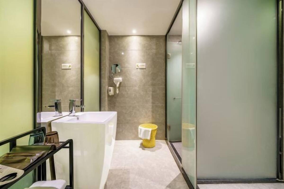 A modern bathroom with a large white sink, a yellow trash bin, and a glass shower enclosure.