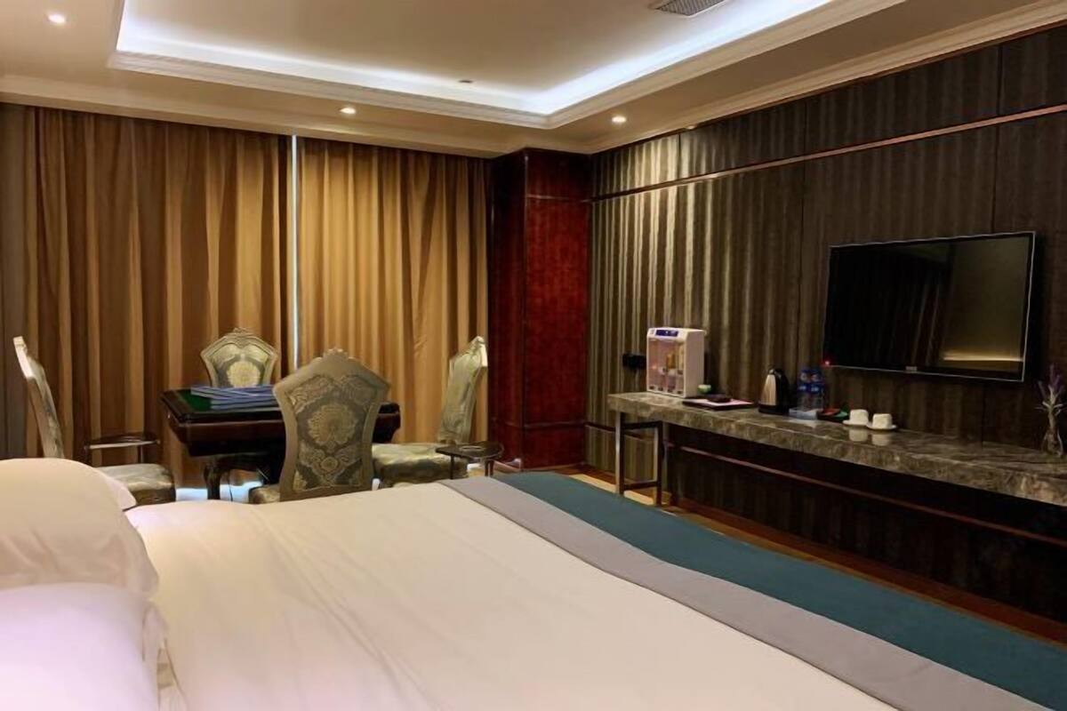 A hotel room with a large bed, a desk with a chair, a TV mounted on the wall, and a minibar.