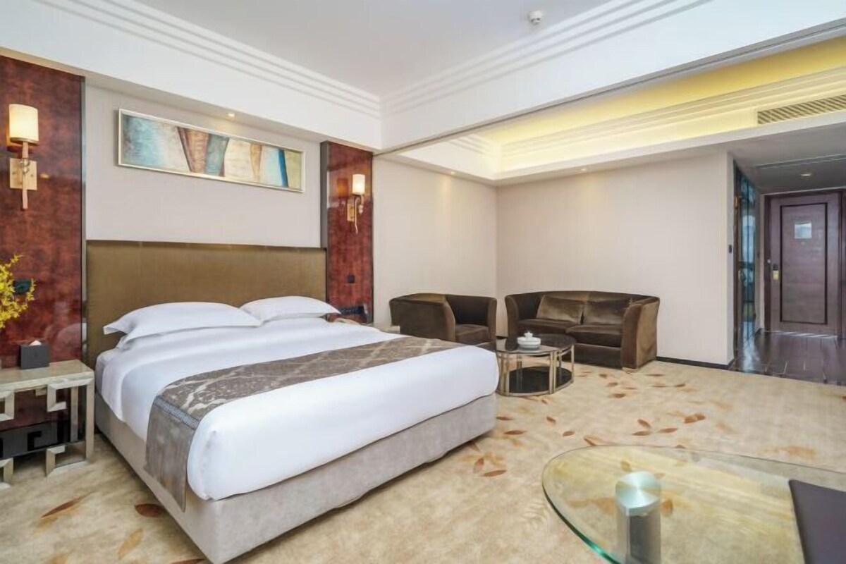 A hotel room with a large bed, a desk, a chair, and a glass coffee table.