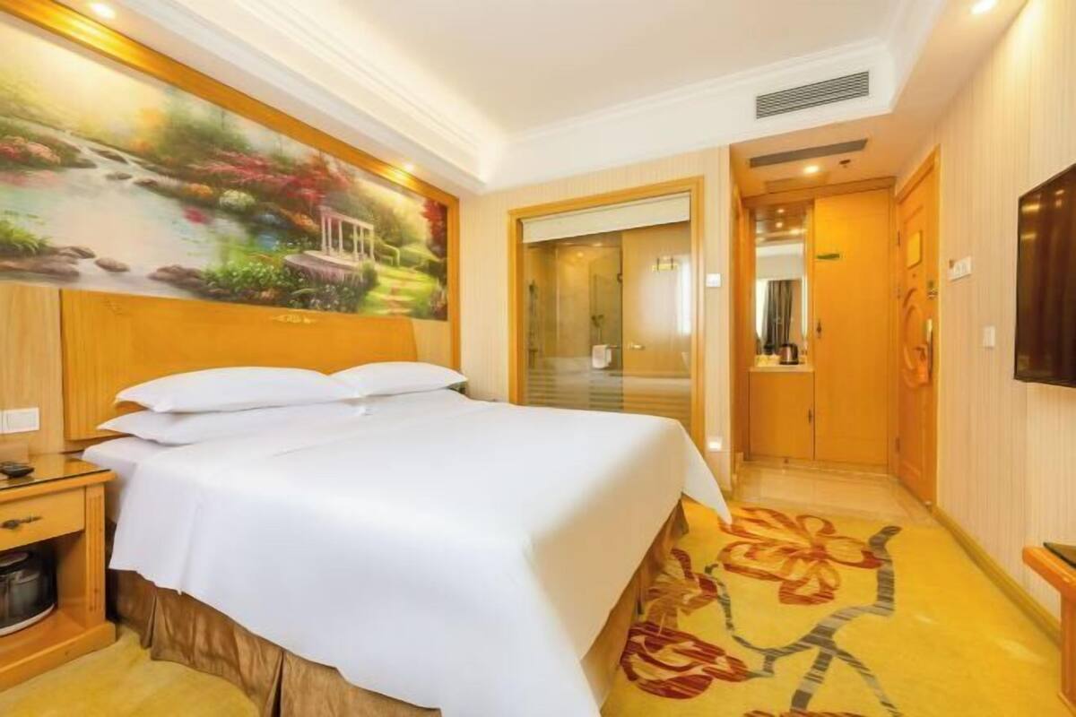 Ein Hotelzimmer mit Bett, Nachttisch, Fernseher, einem Gemälde und einer Badezimmertür.