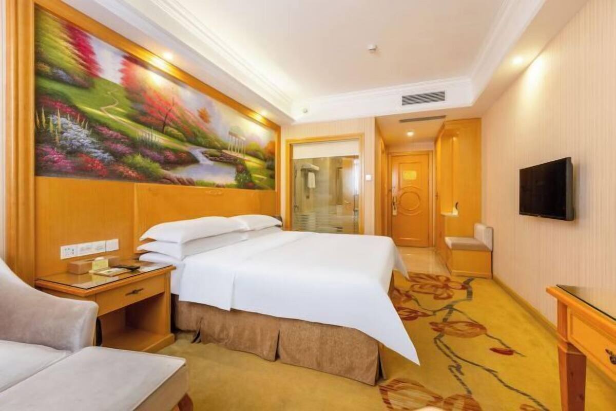 Ein Hotelzimmer mit Bett, Schreibtisch, Stuhl, Fernseher und einem Bild an der Wand.