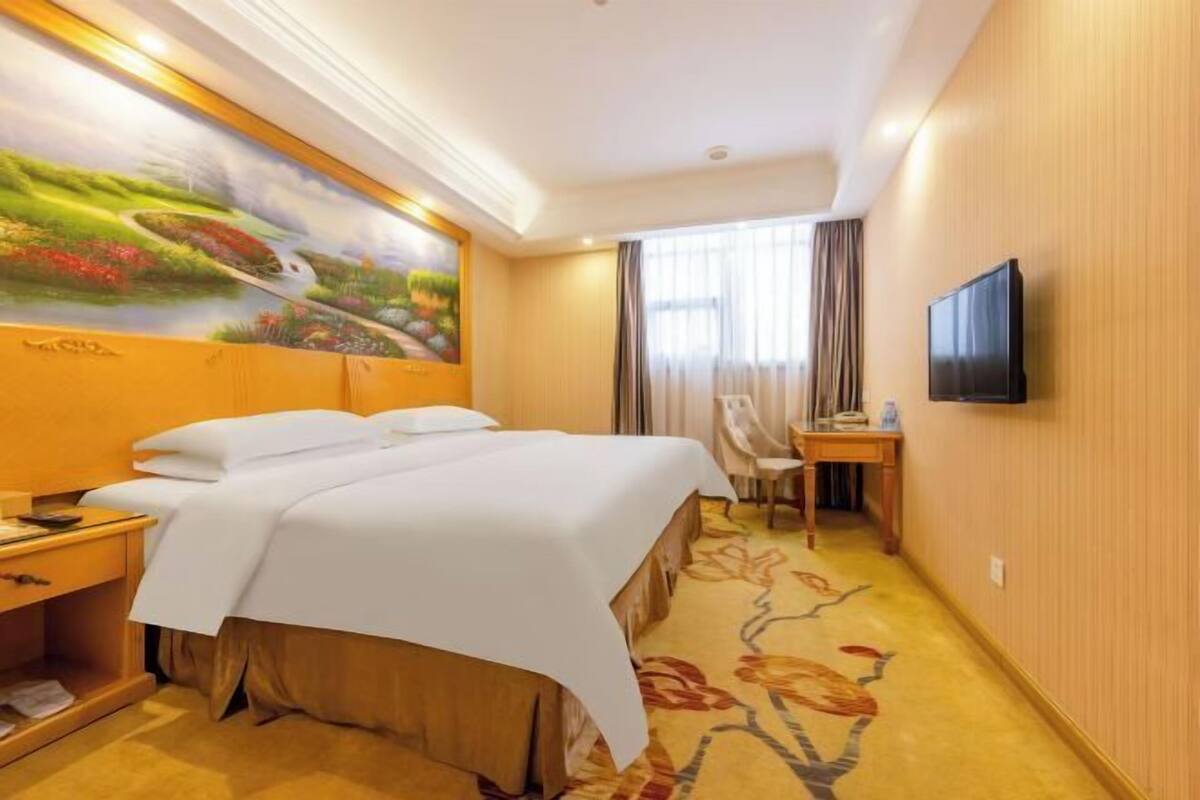 Ein Hotelzimmer mit Bett, Schreibtisch, Stuhl, Fernseher und einem Bild an der Wand.