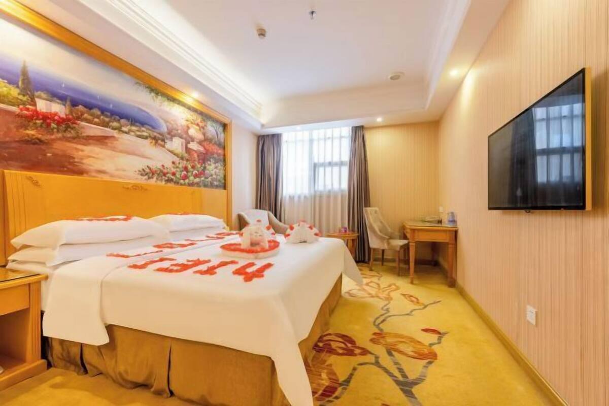 Ein Hotelzimmer mit Bett, Schreibtisch, Stuhl, Fernseher und einem Bild an der Wand.