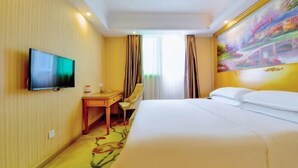 Una habitación de hotel con cama, escritorio, silla, televisor y un cuadro en la pared.