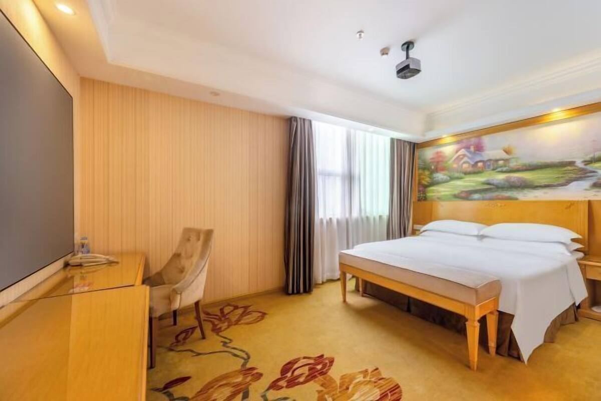 Ein Hotelzimmer mit Bett, Schreibtisch, Stuhl und einem Gemälde an der Wand.
