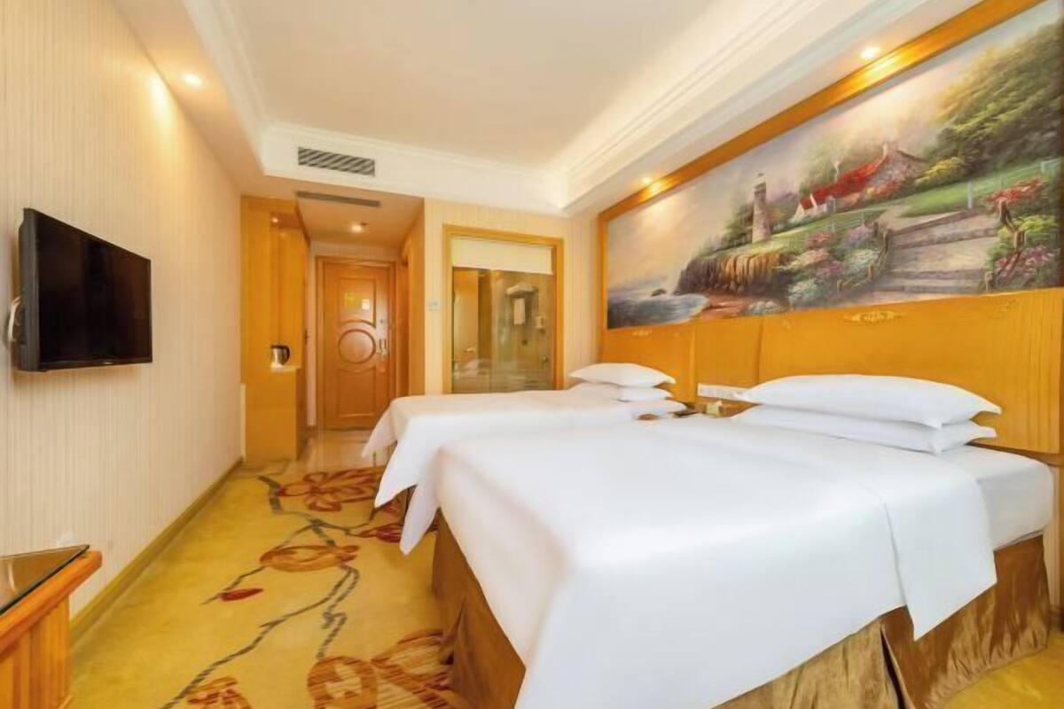 Ein Hotelzimmer mit zwei Betten, einem Fernseher und einem Bild an der Wand.