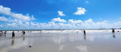 Una playa con gente caminando sobre la arena y el océano al fondo.
