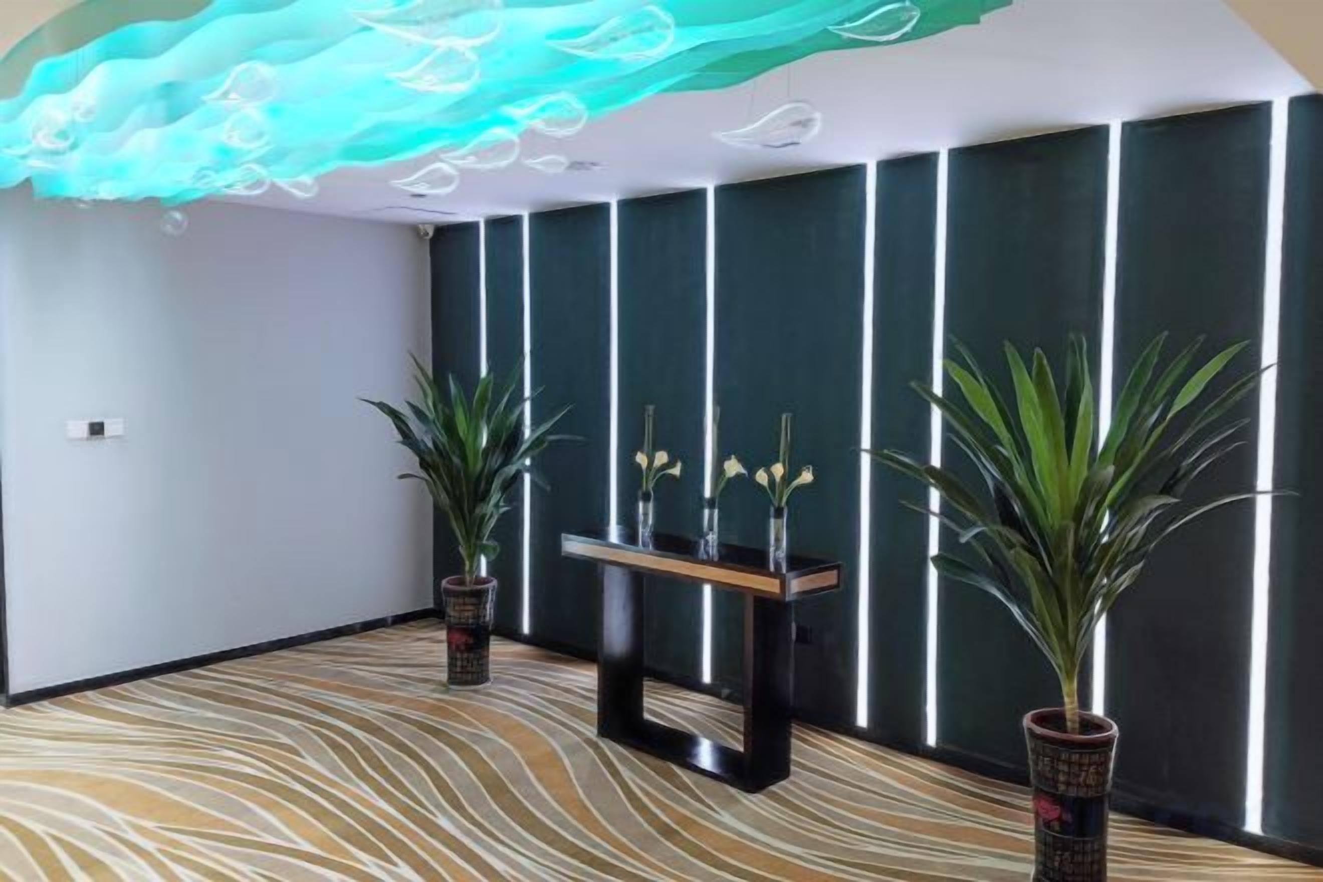 A room with a patterned carpet, a reception desk, potted plants, and a wall with vertical lines.