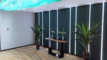A room with a patterned carpet, a reception desk, potted plants, and a wall with vertical lines.