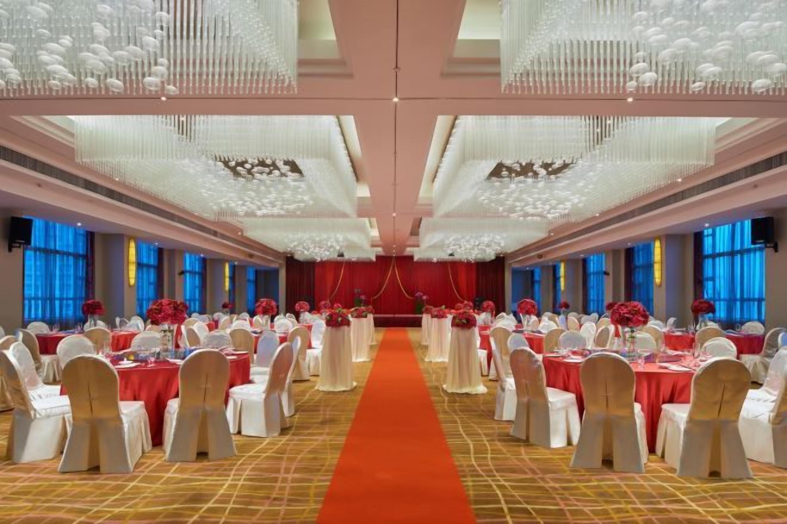 A banquet hall with round tables, a central aisle, and a red carpet.