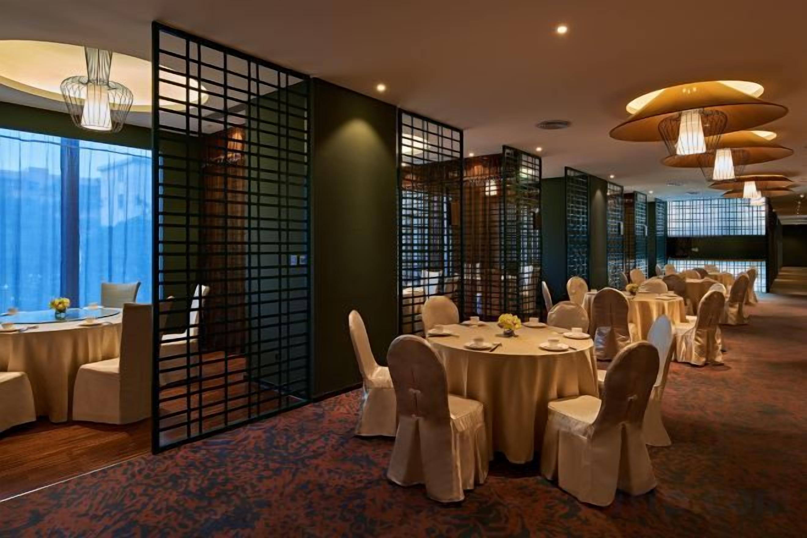 Un salón de banquetes con mesas redondas, sillas y una partición decorativa.