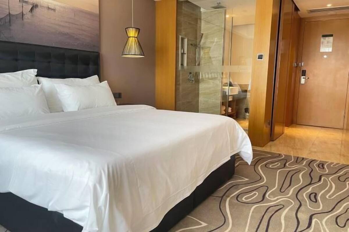 Ett hotellrum med en stor säng, en dusch med glasväggar och en dörr av trä.