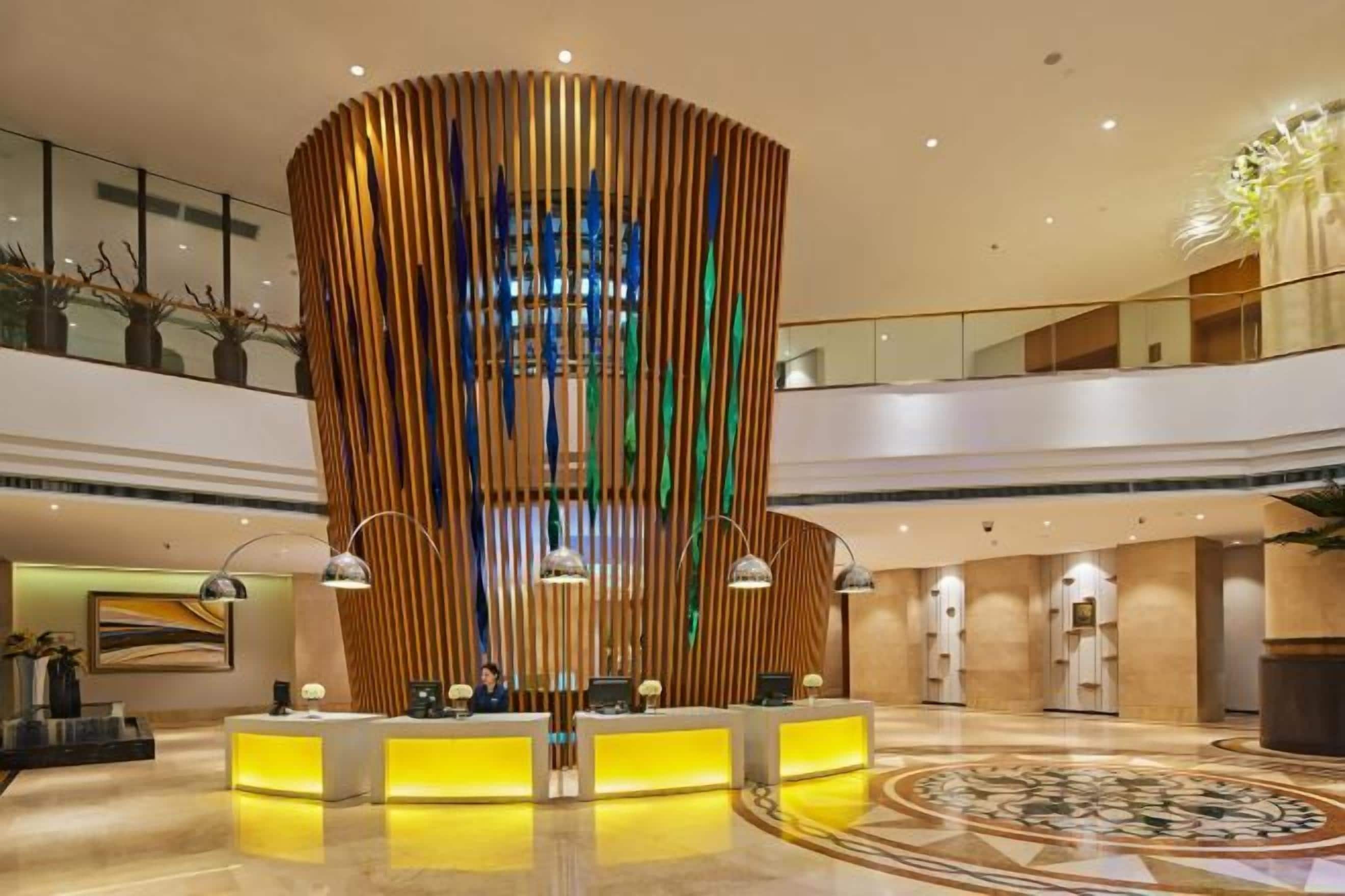 A hotel lobby with a central reception desk, a high ceiling, and a circular patterned floor.