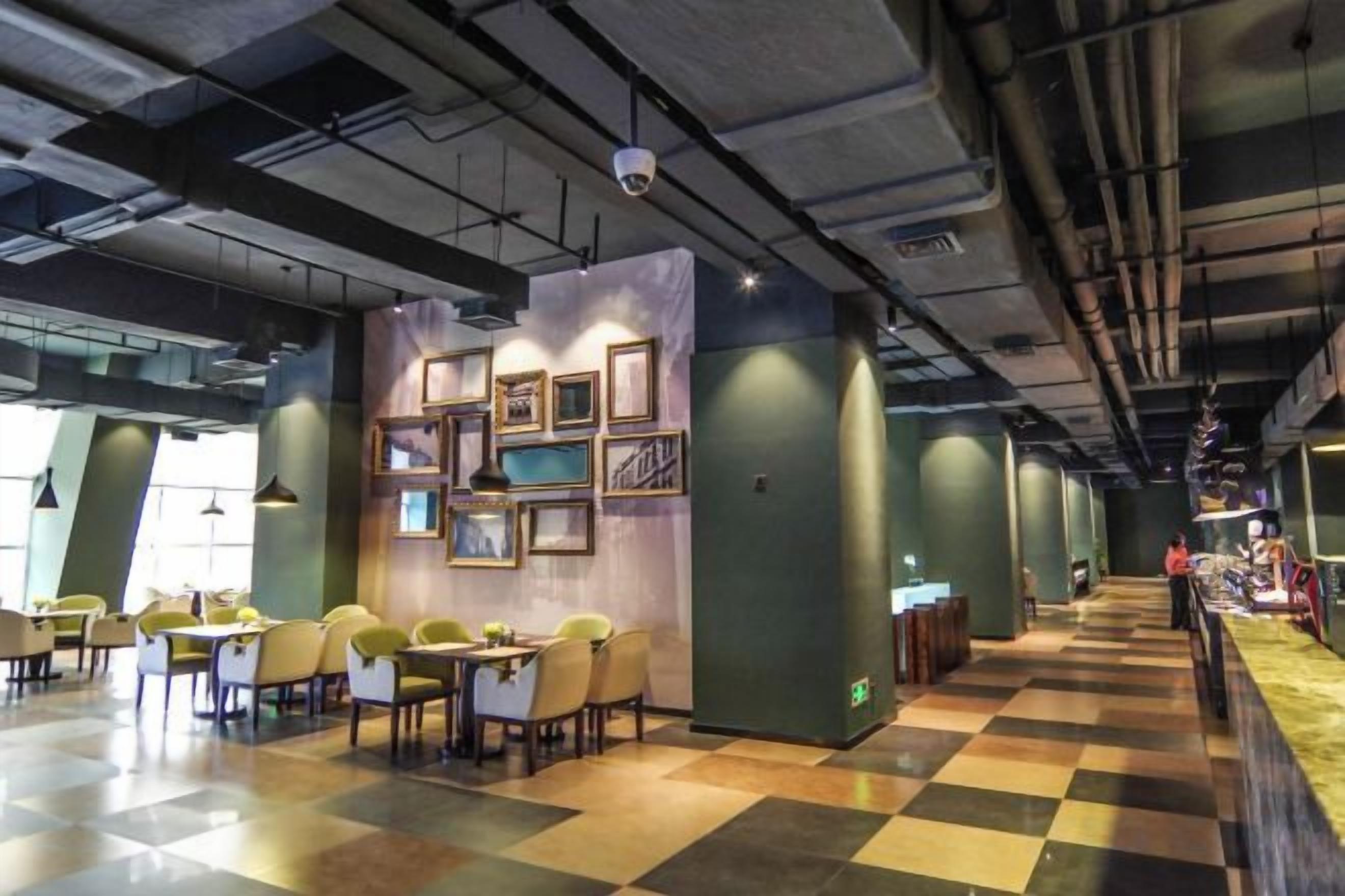 Un espace intérieur spacieux, aménagé avec des tables et des chaises, un mur orné de tableaux encadrés et un sol à carreaux.
