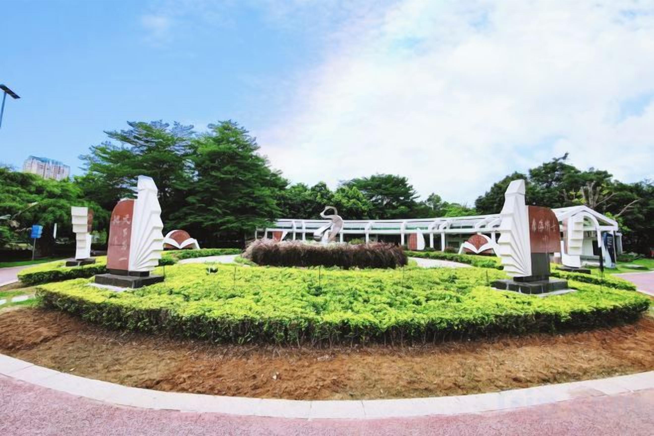 A landscaped area with a central circular garden, two stone monuments, and a building with a white facade in the background.