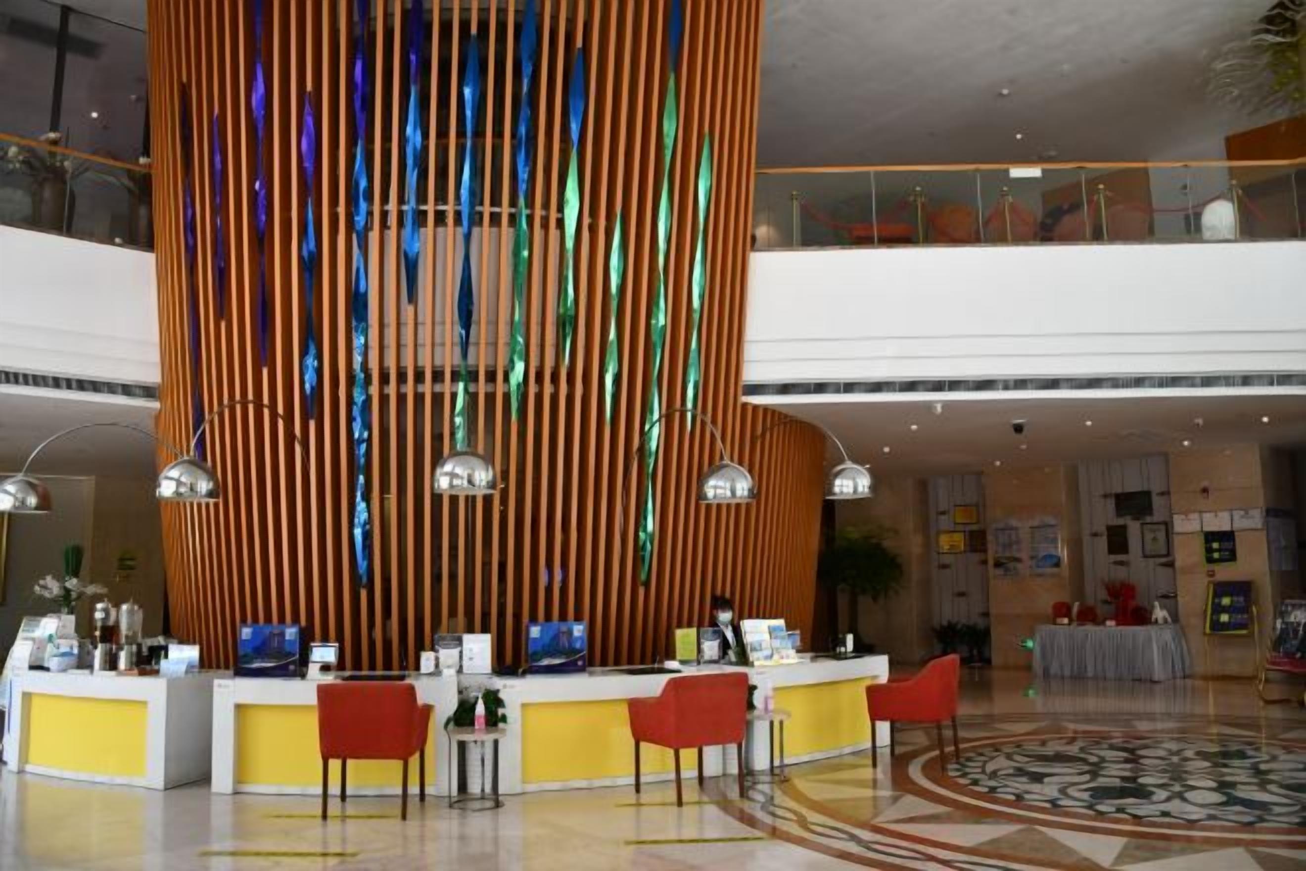 A hotel lobby with a reception desk, multiple chairs, and a decorative vertical panel.