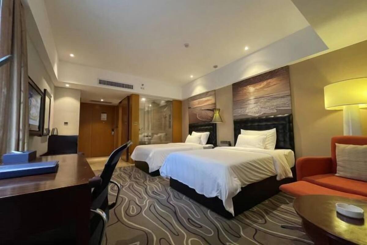 Ett hotellrum med två sängar, ett skrivbord, en stol, en soffa och en lampa.