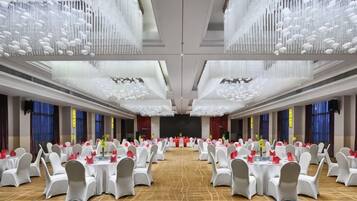 A banquet hall with round tables, chairs, and a stage.