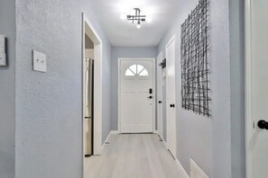 A narrow hallway with light gray walls, a white door at the end, and a ceiling light fixture.