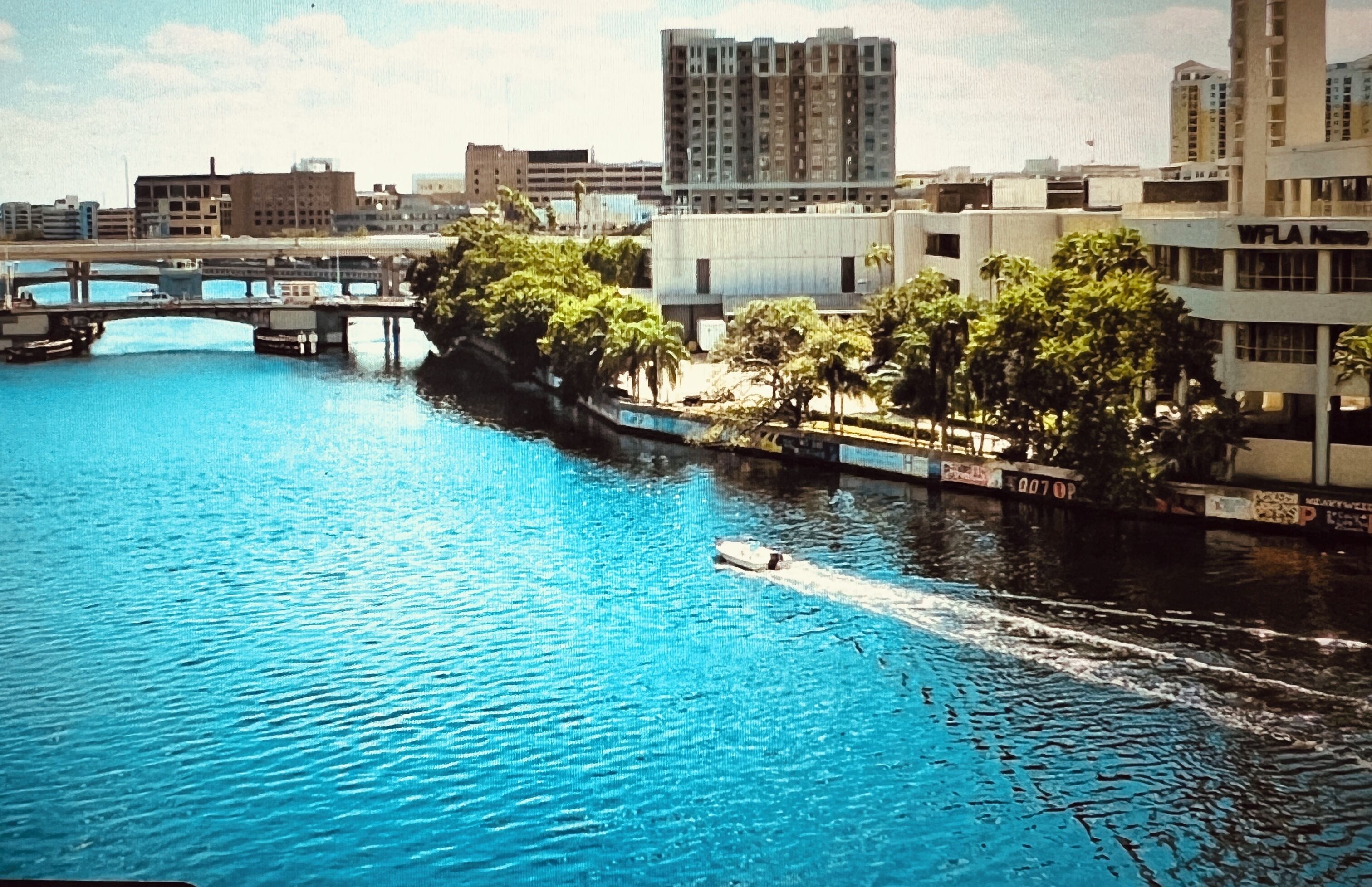 A river with a boat, buildings, and a bridge in the background.