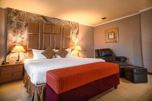 A hotel room with a large bed, two bedside lamps, a leather armchair, and a small ottoman. - Hotel Olympic (Jakarta)