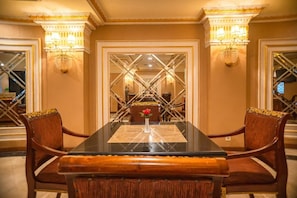 Formal dining room with a classic table set for four, featuring ornate sconces, a decorative mirror, and a chandelier.