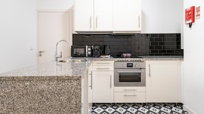 A compact kitchen with a granite countertop, stainless steel sink, a coffee maker, a microwave, and a built-in oven.