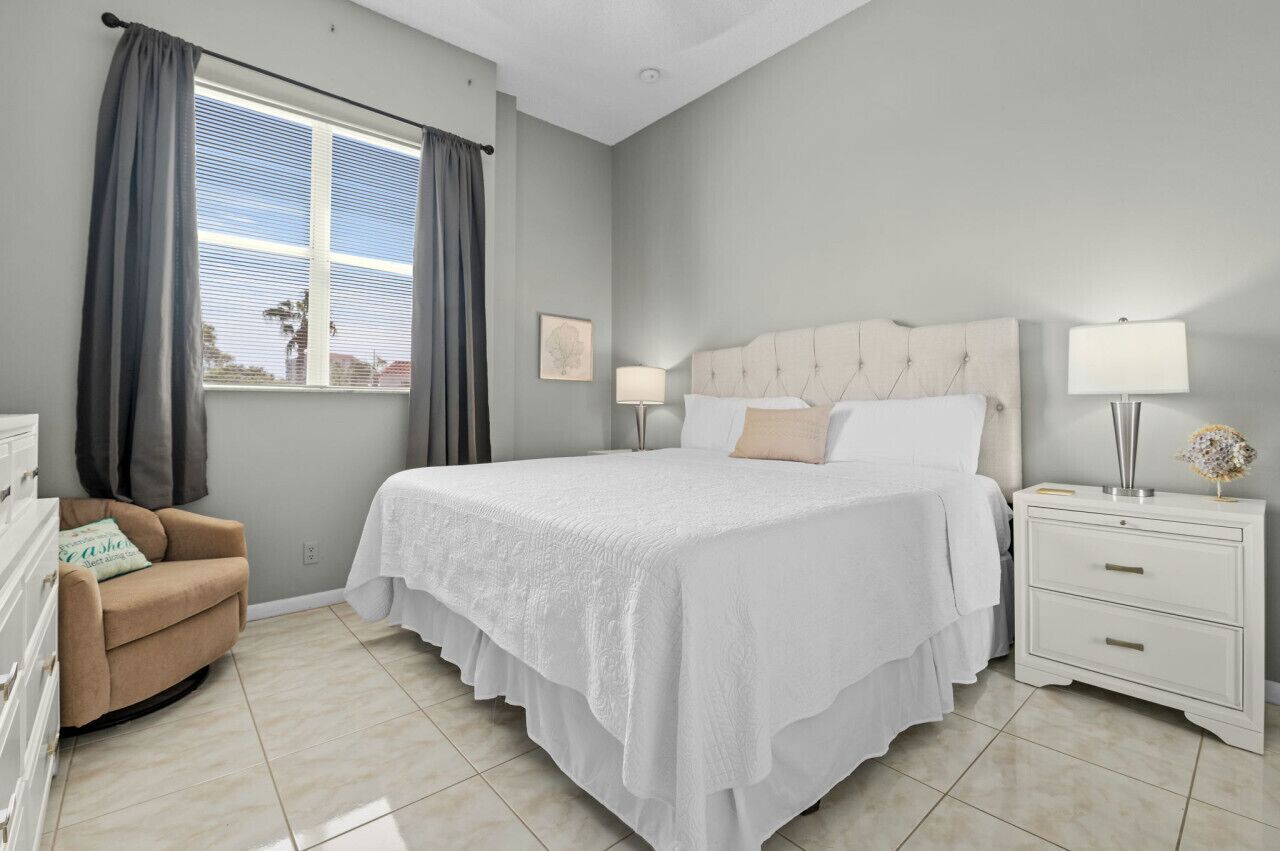 A bedroom with a large bed, two bedside tables, a nightstand, a chair, and a window with curtains.