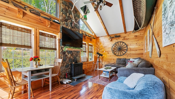 A cozy cabin interior with a stone fireplace, wooden walls, a dining area, and a living room with a blue bean bag. - Charming Farmhouse, Sauna - 4 bedrooms, WiFi, AC in Upper Jay (Upper Jay)